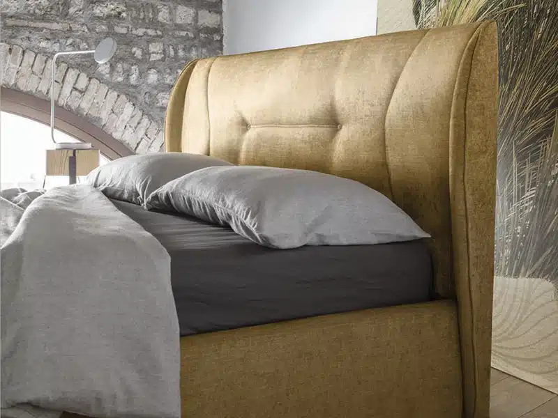 Letto matrimoniale Demetra RigoSalotti in ambientazione minimalista, vista laterale con comodino e lampada da tavolo.
