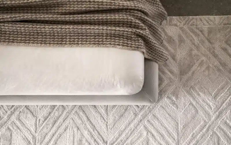 Lenzuola e plaid su letto, tappeto geometrico in tonalità neutre. Design moderno.